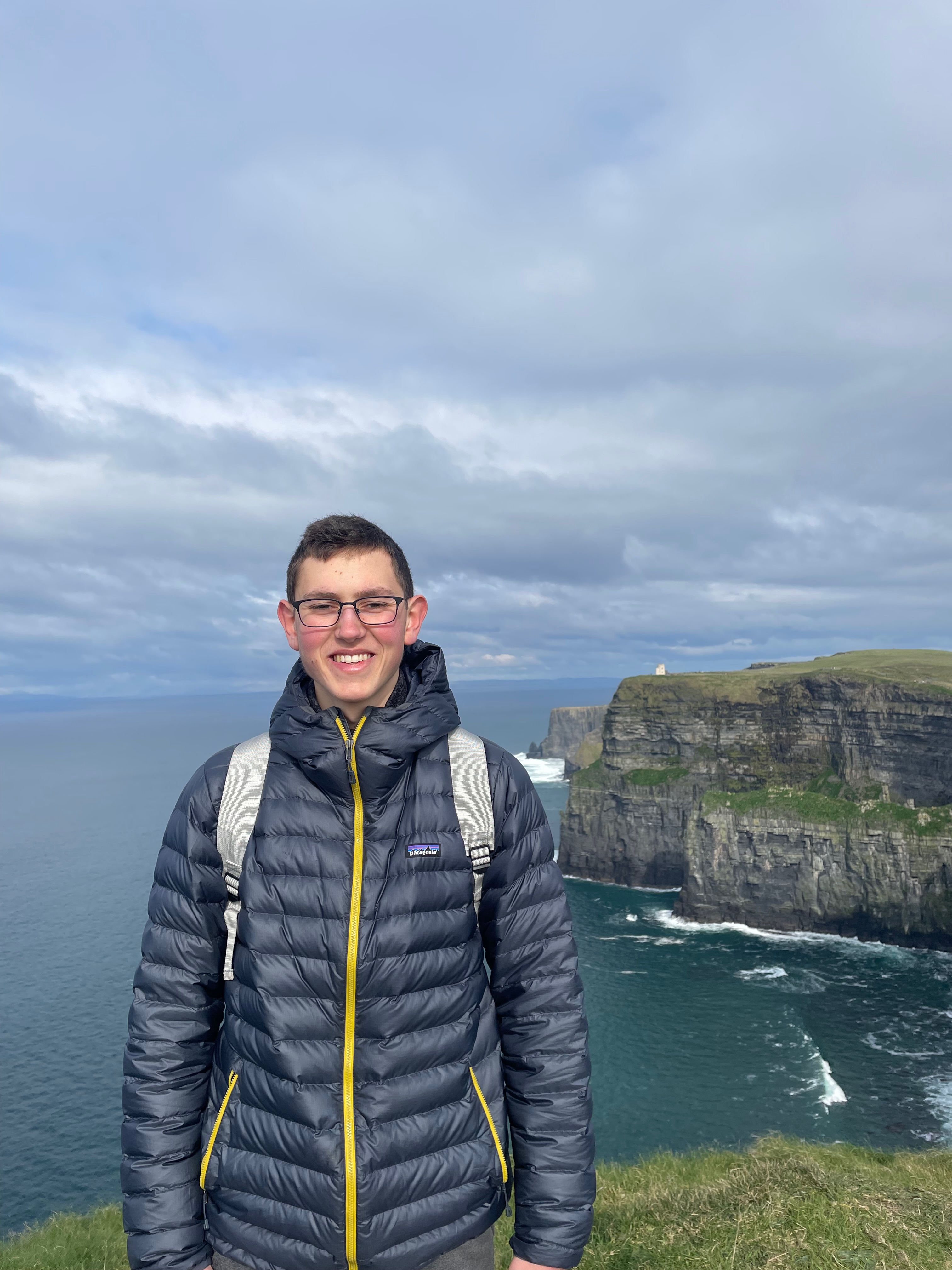 Justin standing in front of a sea vista on the Cliffs of Moher with a Patagonia jacket on.