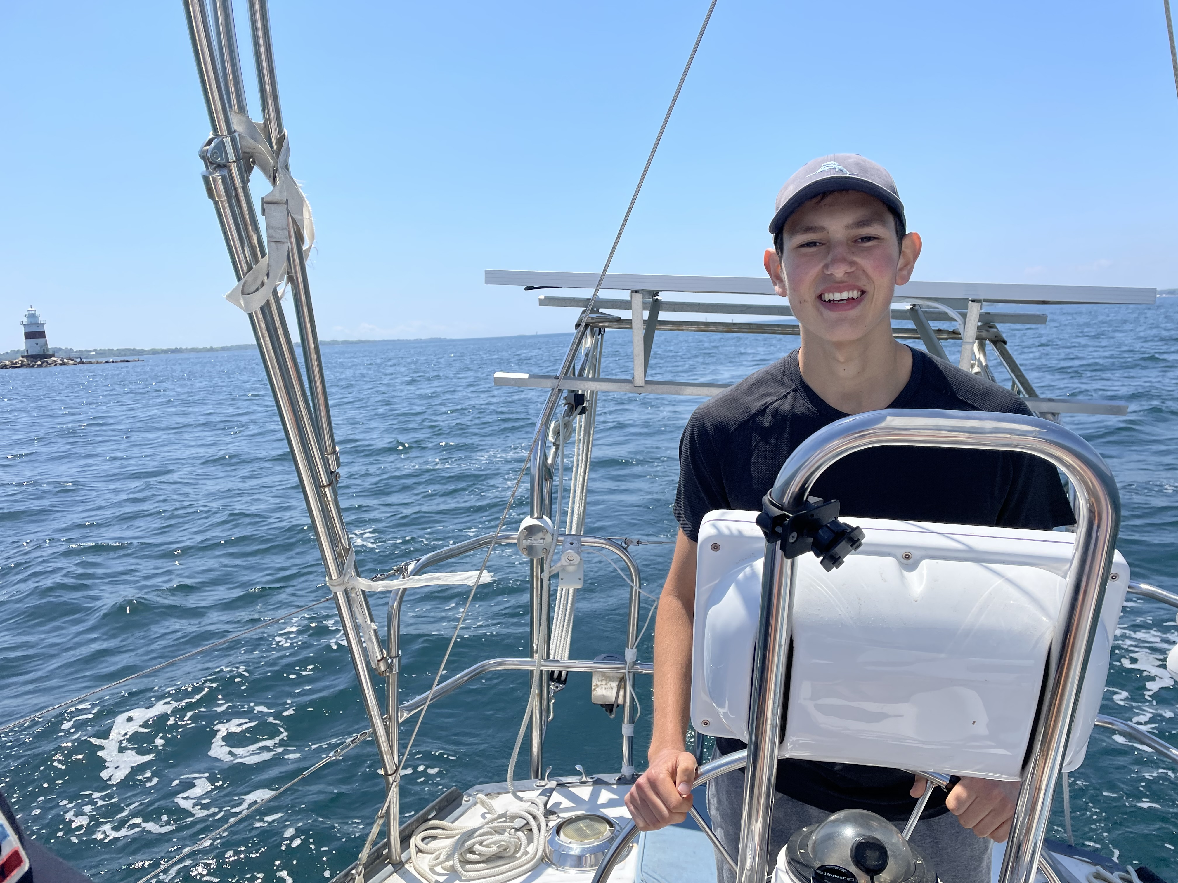 Justin stearing a sailboat with a light house in the background.